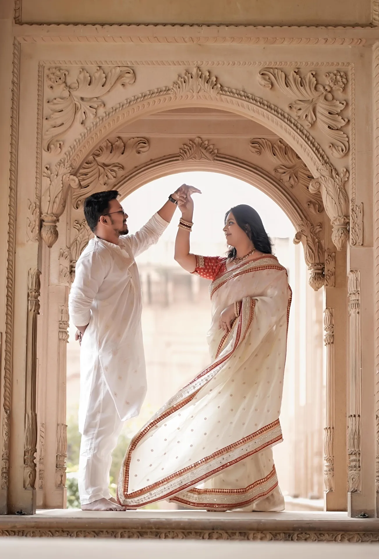 Couple twirling beneath a carved archway during pre-wedding shoot