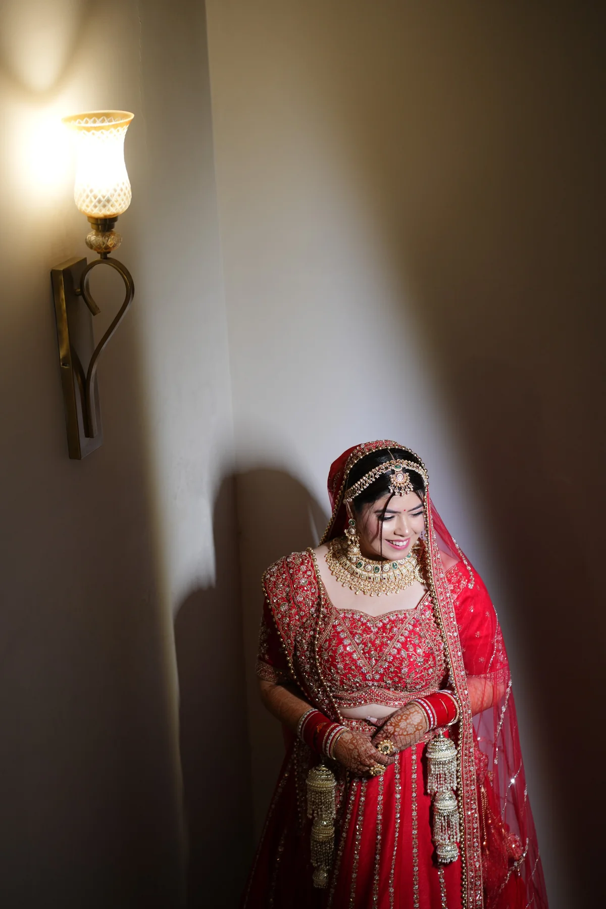 Wide bridal portrait in red lehenga against a textured wall