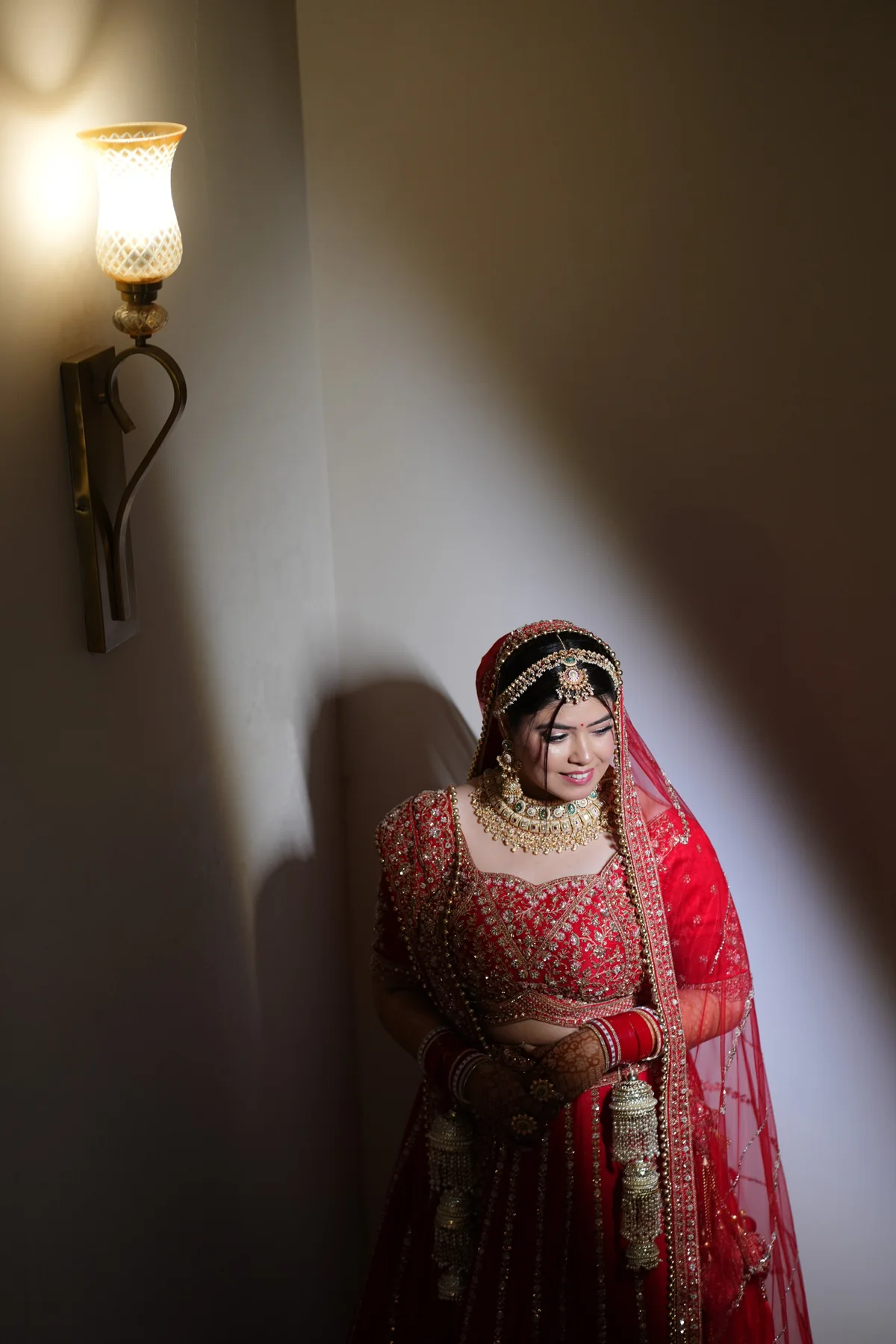 Bride in red lehenga beside a warm wall light